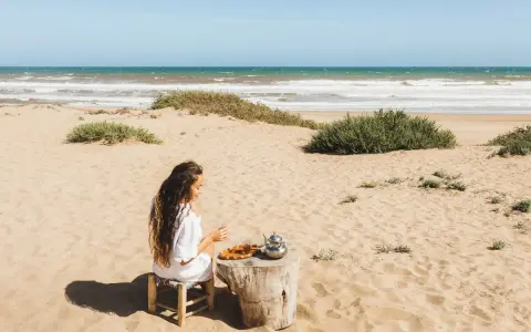 Dziewczyna pije herbatę na plaży, delektując się widokiem na morze w Tunezji.