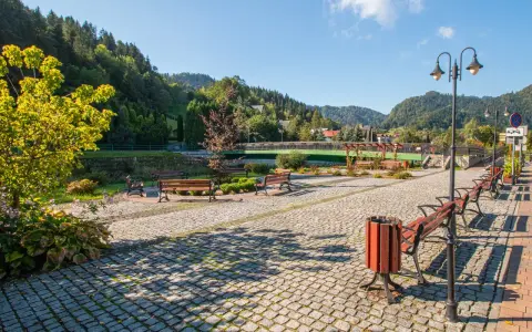 Słoneczna promenada Szczawnica z kamienną nawierzchnią, ławkami i latarniami, otoczona zielenią i górami.