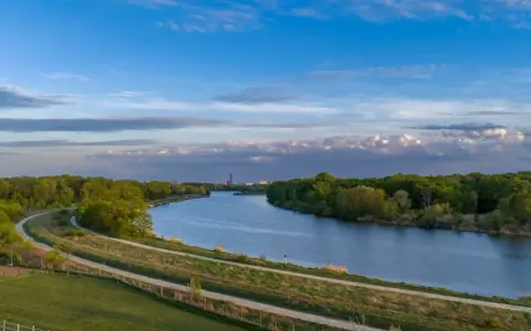 Wisła, jaka rzeka płynie przez Kraków, meandruje wśród zieleni. W oddali widać miejską panoramę.