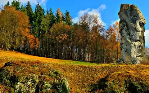 Jesienna trasa Maczugi Herkulesa. Wysoka skała góruje nad złotymi polami i kolorowym lasem.
