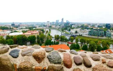 Widok na nowoczesne centrum Wilna z rzeką i mostami, a na pierwszym planie kamienny murek.