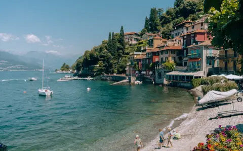 Urokliwa plaża w Bergamo, z kolorowymi domkami na wzgórzu, łodziami na wodzie i dziećmi bawiącymi się nad brzegiem.