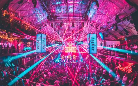 Tłum ludzi tańczy w rytm muzyki pod neonowymi światłami i laserami. To niezapomniane ibiza imprezy w klubie pełnym energii.