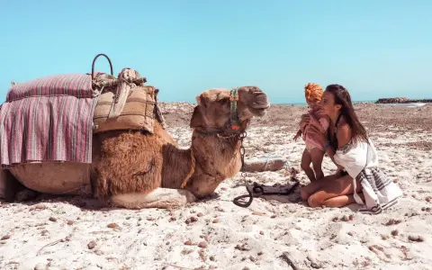 Kobieta z dzieckiem na plaży w Tunezji, obok wielbłąd. Niezapomniane tunezja atrakcje.