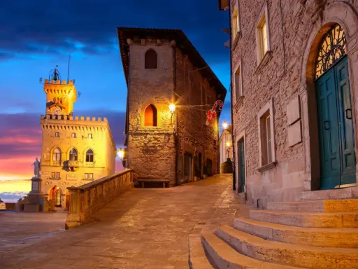 Kamienne uliczki i wieże w San Marino o zmierzchu, z kolorowym niebem i oświetlonymi budynkami.