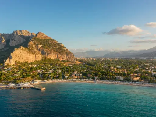 Malownicze **Palermo plaża** z turkusową wodą, skalistym klifem i miastem w tle.