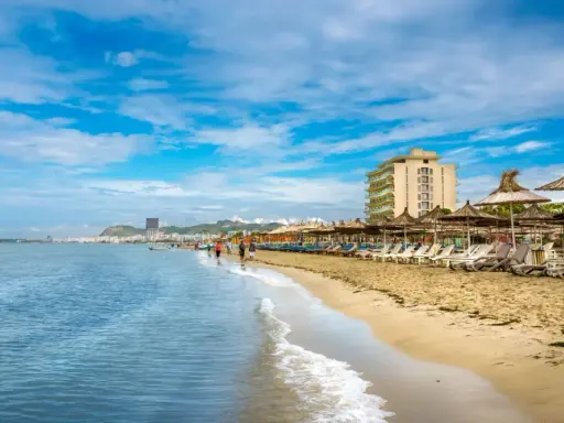 Słoneczna plaża w Golem, Albania, z rzędem leżaków i parasoli. W oddali widać hotel i miasto.