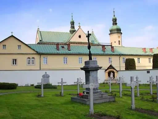Cmentarz przy klasztorze w Czerniej. W tle żółty budynek z zielonym dachem i wieżą.