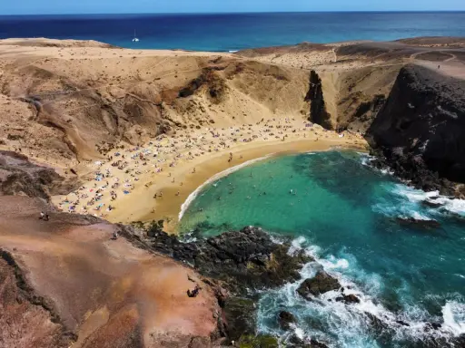 Rajska plaża z turkusową wodą i ludźmi opalającymi się na piasku. To idealne miejsce, co zobaczyć na Lanzarote, by poczuć słońce i odpocząć.