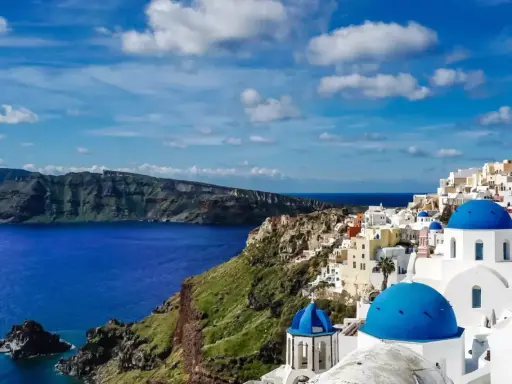 Widok na białe domy z niebieskimi kopułami na klifie, morze i góry. Klasyczny krajobraz Grecji, Santorini.