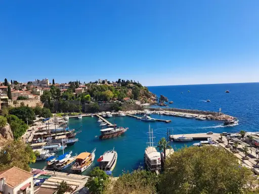 Widok na port w Antalyi, gdzie cumują liczne łodzie i jachty. W tle widać miasto i błękitne morze. Idealne miejsce, by zobaczyć, co oferuje Antalya.