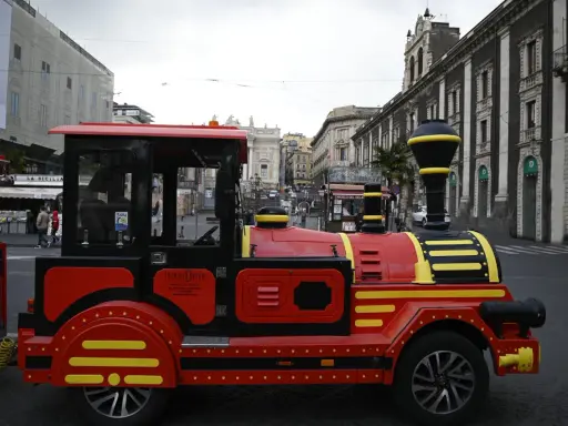 Czerwony turystyczny pociąg na ulicach Sycylii, oferujący nietypową komunikację miejską.