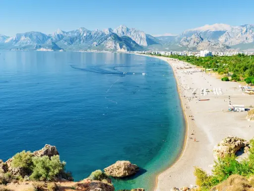 Słoneczna riwiera turecka Antalya kusi turkusowym morzem i piaszczystą plażą, w tle majestatyczne góry.