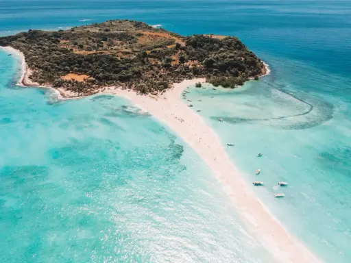Rajska plaża na Nosy Be, z turkusową wodą, piaszczystym cyplem i łodziami.