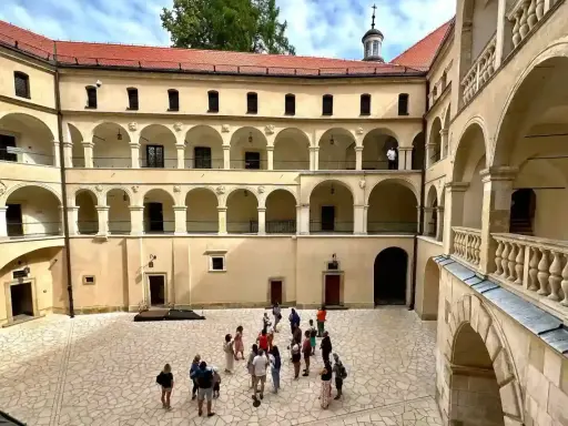 Dziedziniec zamku Ojcowie z arkadowymi krużgankami, gdzie spacerują turyści.