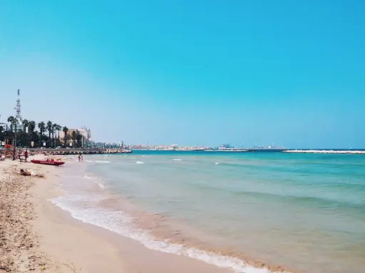 Słoneczna bari plaża z turkusową wodą i palmami w tle. Czerwona łódź ratownicza na piasku.
