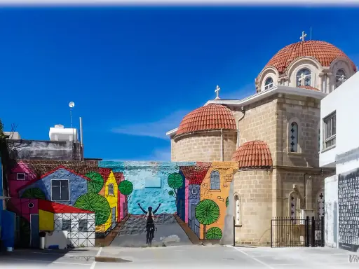 Kolorowy mural z rowerzystą i domkami na tle kościoła z kopułami. Pafos Cypr centrum.
