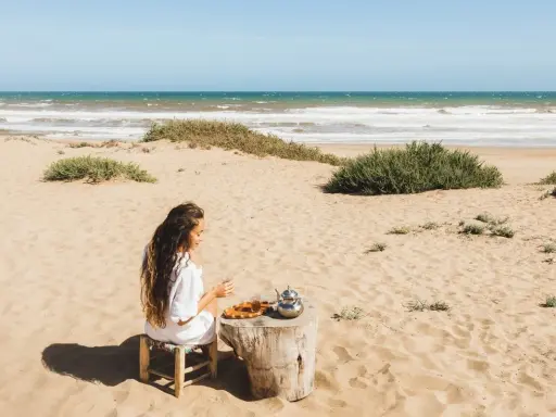 Dziewczyna pije herbatę na plaży, delektując się widokiem na morze w Tunezji.