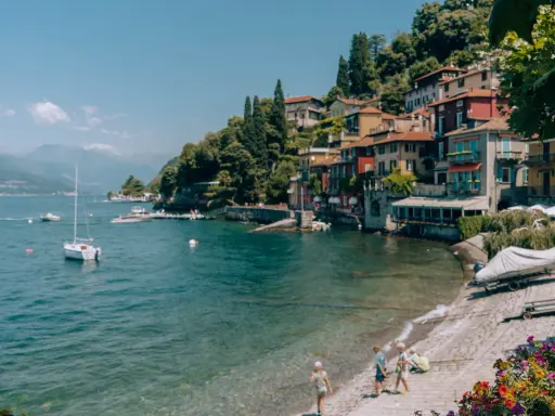 Urokliwa plaża w Bergamo, z kolorowymi domkami na wzgórzu, łodziami na wodzie i dziećmi bawiącymi się nad brzegiem.