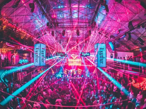 Tłum ludzi tańczy w rytm muzyki pod neonowymi światłami i laserami. To niezapomniane ibiza imprezy w klubie pełnym energii.