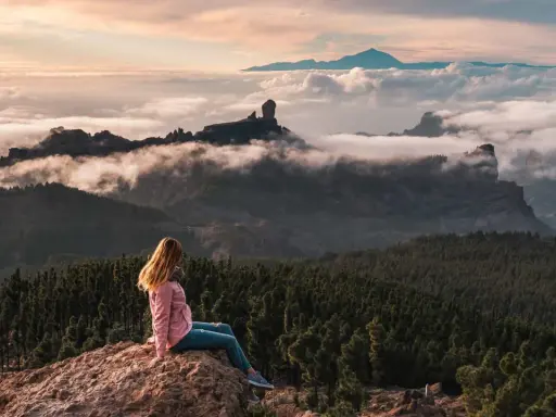 Kobieta siedzi na skale, podziwiając mgły i góry na Gran Canarii. W oddali widać Roque Nublo.