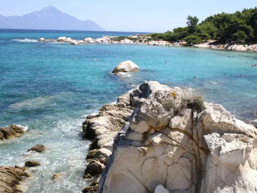 Piękne, turkusowe morze i skaliste wybrzeże. Ludzie kąpią się i opalają na plaży. To idealne chalkidiki atrakcje dla każdego.