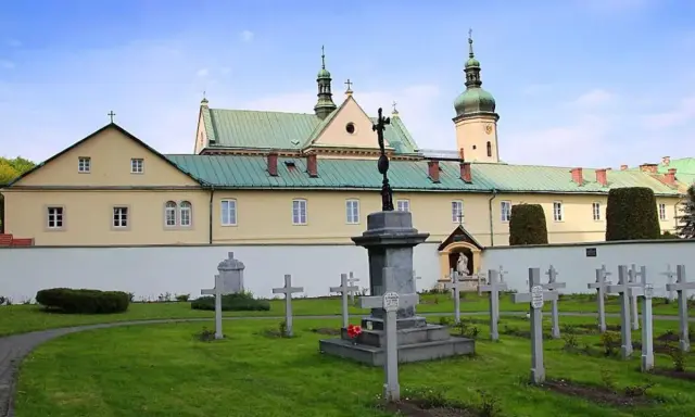 Cmentarz przy klasztorze w Czerniej. W tle żółty budynek z zielonym dachem i wieżą.