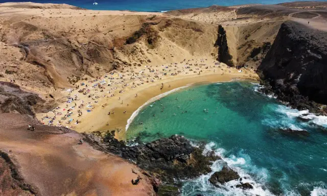 Rajska plaża z turkusową wodą i ludźmi opalającymi się na piasku. To idealne miejsce, co zobaczyć na Lanzarote, by poczuć słońce i odpocząć.