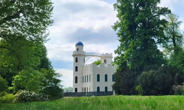 Biały zamek z niebieską kopułą, otoczony zielenią. Idealne miejsce na odkrywanie nietypowych atrakcji w Berlinie.
