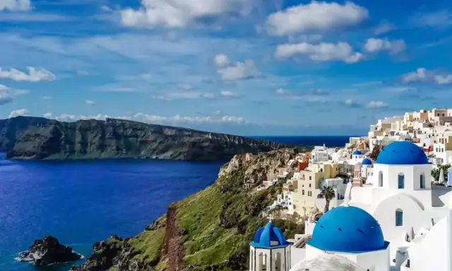 Widok na białe domy z niebieskimi kopułami na klifie, morze i góry. Klasyczny krajobraz Grecji, Santorini.