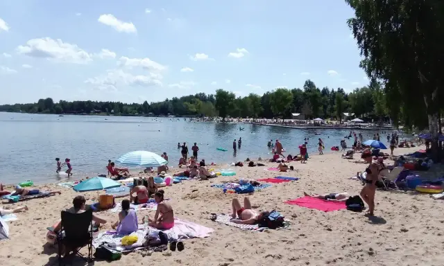 Słoneczny dzień nad **jaworznem jeziorem**. Ludzie odpoczywają na plaży, kąpią się i opalają.