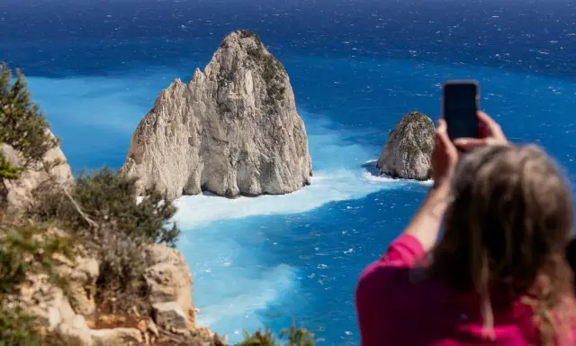Widok na turkusowe morze i skaliste wysepki. Kobieta robi zdjęcie telefonem. Czy Zakynthos warto odwiedzić? Tak!