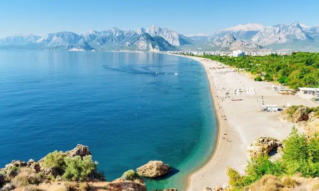 Słoneczna riwiera turecka Antalya kusi turkusowym morzem i piaszczystą plażą, w tle majestatyczne góry.