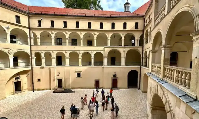 Dziedziniec zamku Ojcowie z arkadowymi krużgankami, gdzie spacerują turyści.