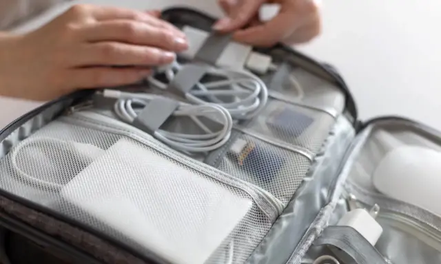 W torbie podróżnej schludnie ułożone kable, ładowarki i powerbank do samolotu. Dłonie porządkują zawartość.