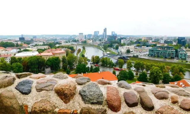 Widok na nowoczesne centrum Wilna z rzeką i mostami, a na pierwszym planie kamienny murek.