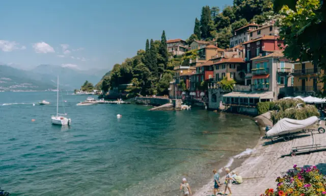 Urokliwa plaża w Bergamo, z kolorowymi domkami na wzgórzu, łodziami na wodzie i dziećmi bawiącymi się nad brzegiem.