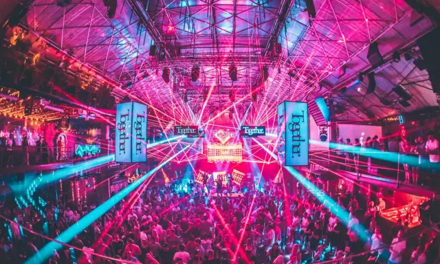 Tłum ludzi tańczy w rytm muzyki pod neonowymi światłami i laserami. To niezapomniane ibiza imprezy w klubie pełnym energii.