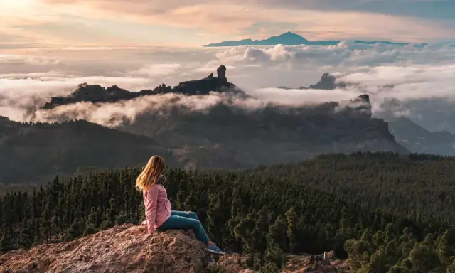 Kobieta siedzi na skale, podziwiając mgły i góry na Gran Canarii. W oddali widać Roque Nublo.
