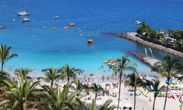 Słoneczne gran canaria plaże pełne ludzi, łodzi i palm. Błękitna woda zaprasza do kąpieli i wodnych zabaw.