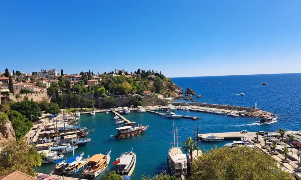 Widok na port w Antalyi, gdzie cumują liczne łodzie i jachty. W tle widać miasto i błękitne morze. Idealne miejsce, by zobaczyć, co oferuje Antalya.