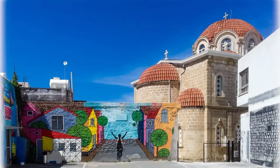 Kolorowy mural z rowerzystą i domkami na tle kościoła z kopułami. Pafos Cypr centrum.