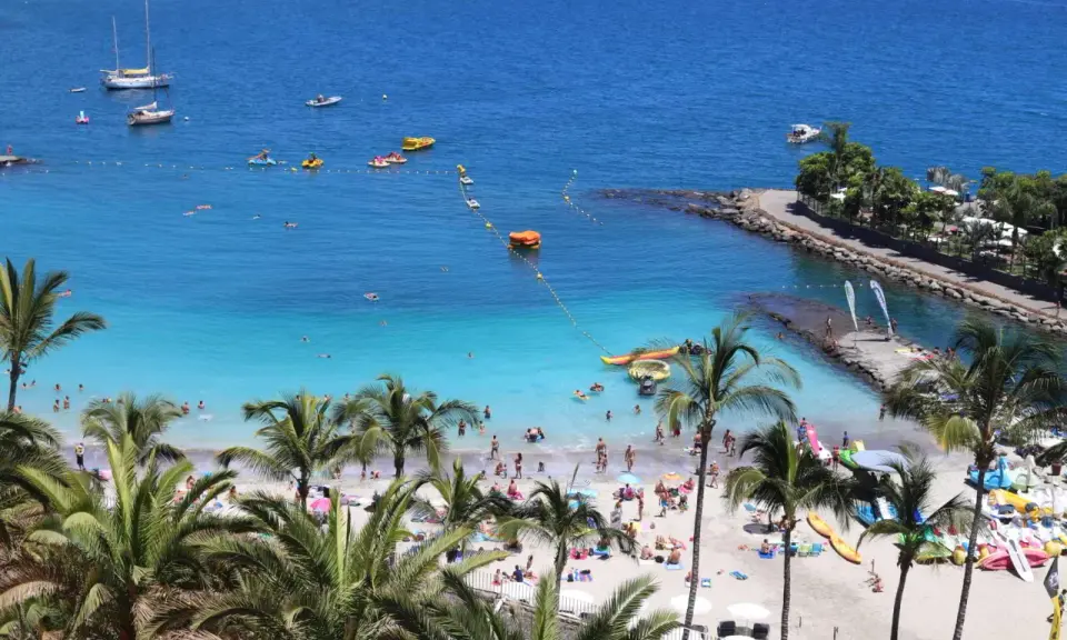 Słoneczne gran canaria plaże pełne ludzi, łodzi i palm. Błękitna woda zaprasza do kąpieli i wodnych zabaw.