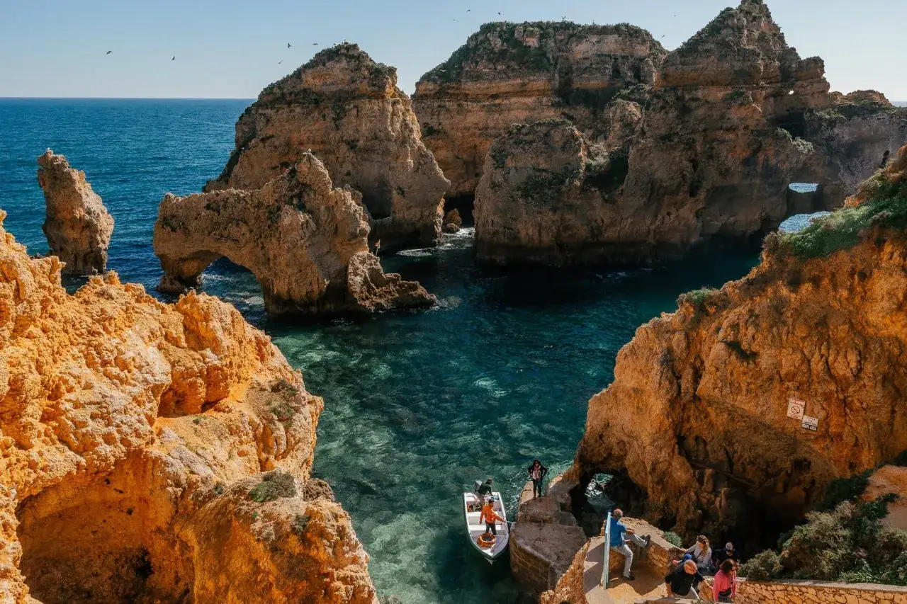 Malownicze klify i jaskinie w Algarve, gdzie warto zobaczyć łódź z turystami w krystalicznie czystej wodzie.
