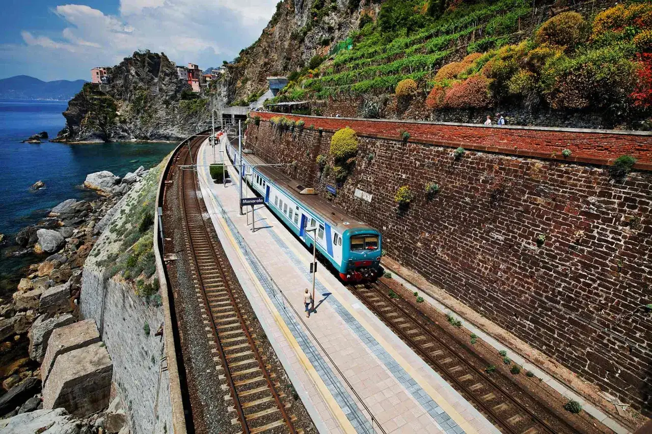Pociąg z Mediolanu nad morze dociera do stacji Manarola. Widok na tory, morze i kolorowe domy na klifie.