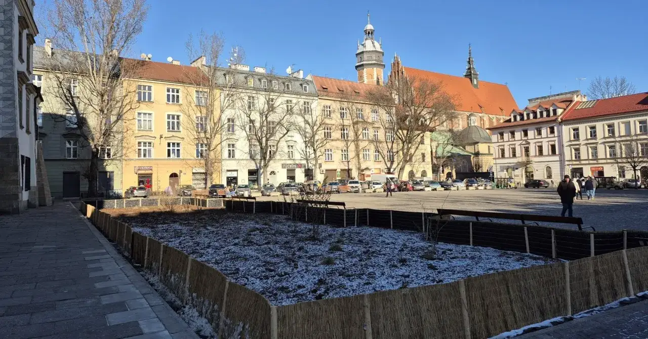 Zimowy rynek na Kazimierzu w Krakowie, z placem w trakcie przygotowań do wiosny. W tle kamienice i kościół.