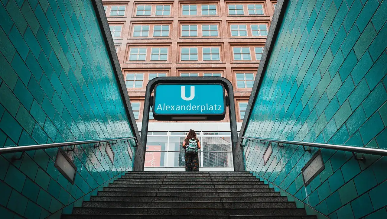Schody do metra U Alexanderplatz w Berlinie, z turystką i charakterystycznymi turkusowymi kafelkami. Nietypowe atrakcje Berlina czekają!