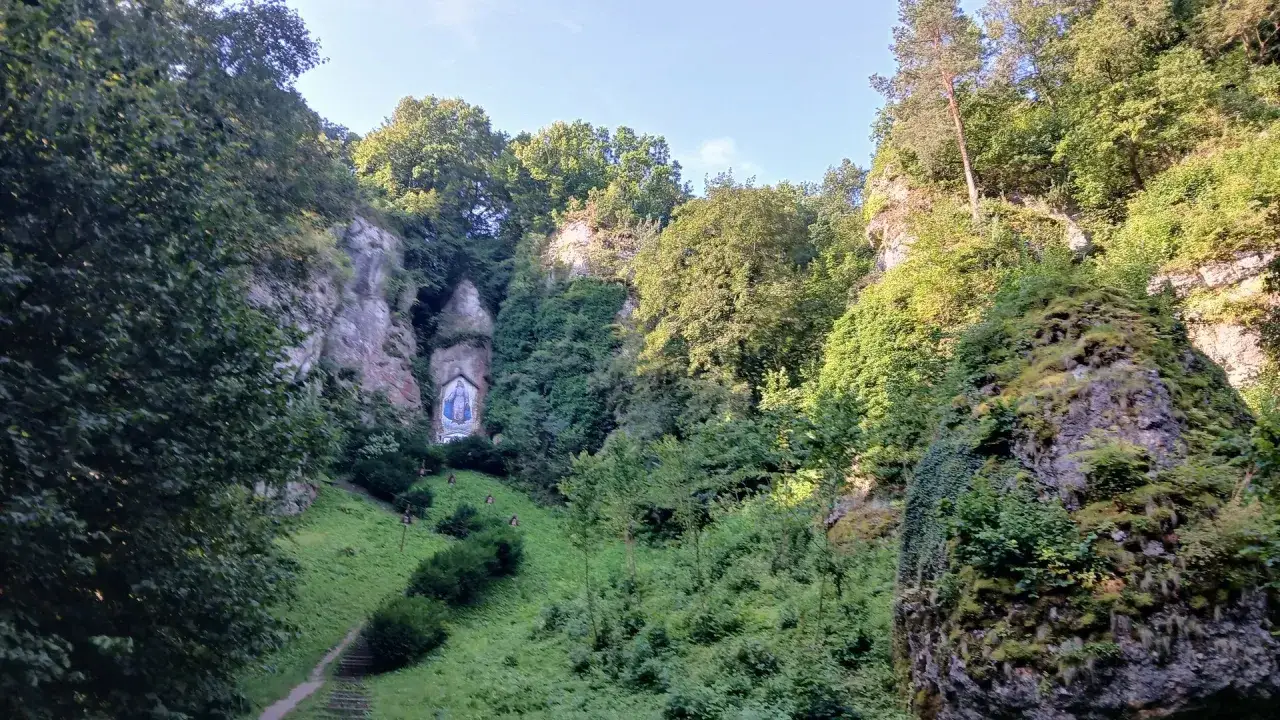Malownicza dolinka mnikowska z kapliczką Matki Boskiej w skalnej grocie. Ścieżka prowadzi przez zielone zbocza porośnięte drzewami.