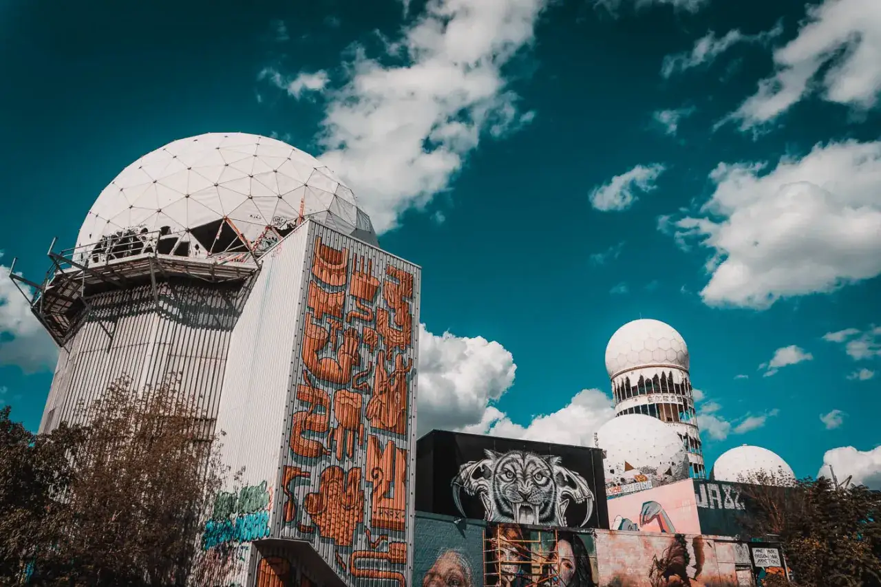 Berlińskie nietypowe atrakcje: opuszczona stacja nasłuchowa z kopułami i kolorowym graffiti, w tym wizerunek tygrysa.