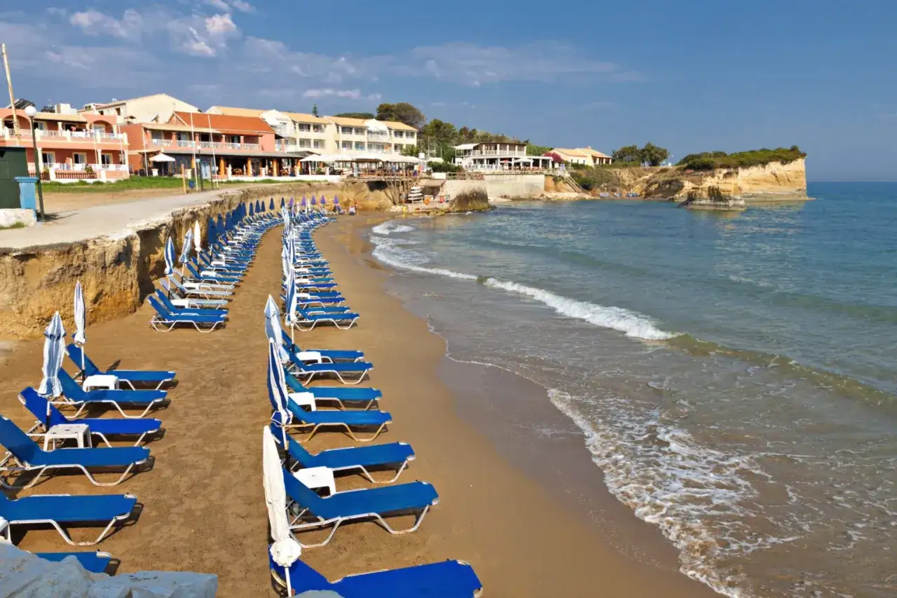 Piękna plaża na wyspie Korfu, z rzędami leżaków i parasoli, zaprasza do odpoczynku nad turkusowym morzem.